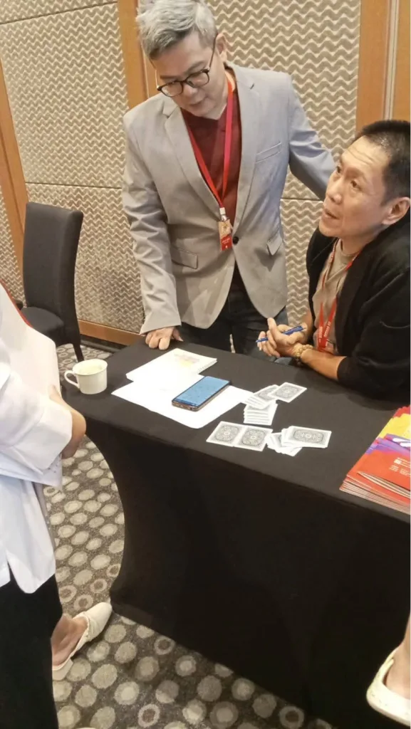 猫哥正在指导一名手忙脚乱的学员进行现场奇门遁甲占卜，桌面上摆放着占卜用的牌卡