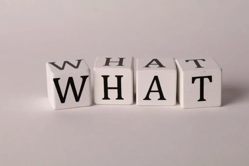 白色木制字母块拼成“WHAT”单词，象征探索命理风水的核心定义与人生疑惑