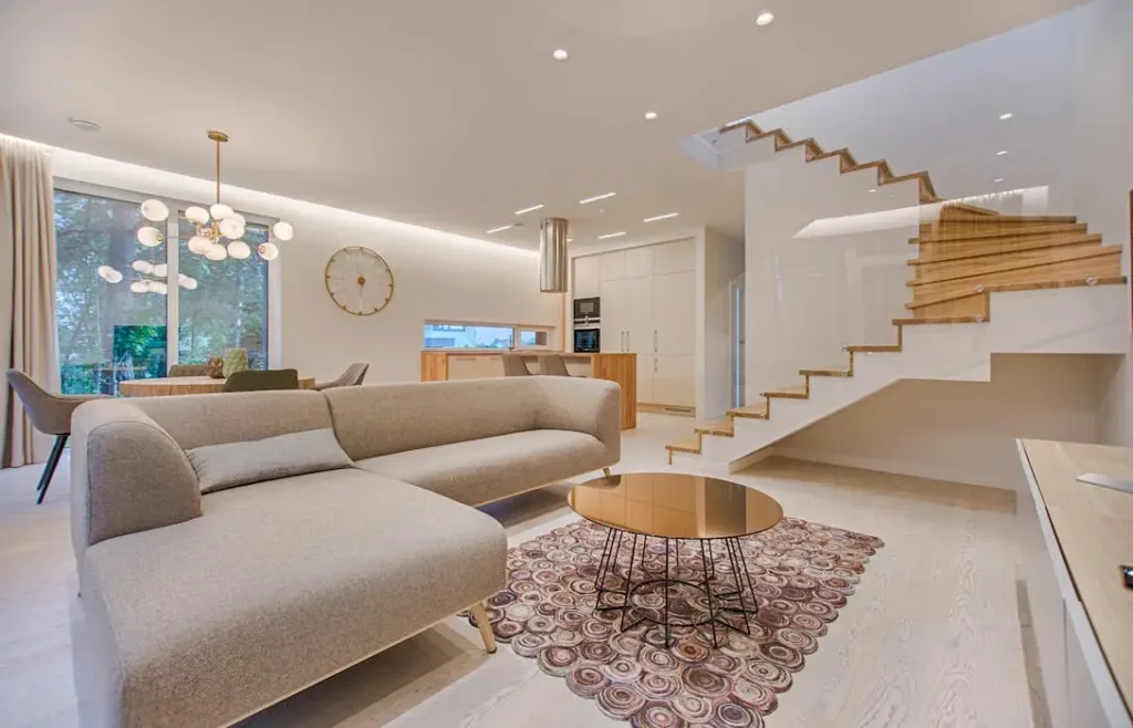 Invisible Architecture: Chi Flow with Open Staircases - 猫哥风水|马来西亚风水・紫微斗数・奇门遁甲 A spacious luxury living room featuring a modern wooden staircase with glass railing. This open layout allows for optimal Chi flow between floors, while the round coffee table and soft sofa shapes promote smooth energy circulation.
